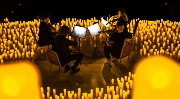 violinists play while surrounded by candles